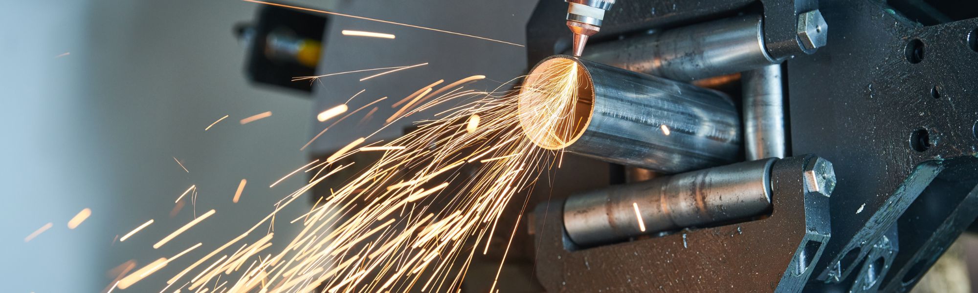 Sparks flying off of machining tool cutting through a metal pipe.