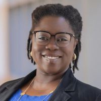 Woman wearing glasses and black blazer with blue shirt smiling