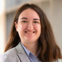 Woman wearing light gray blazer and blue shirt smiling