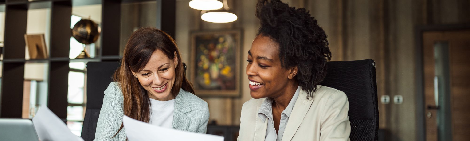 Two professional women discussing paperwork held between them.