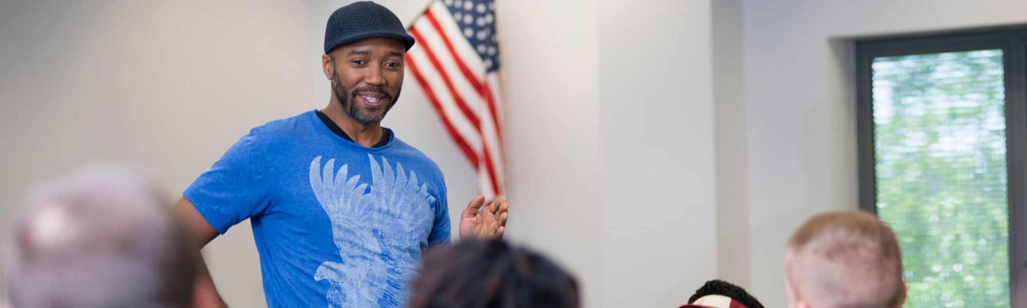 Professor speaking to his students with an American flag behind him on the classroom wall.